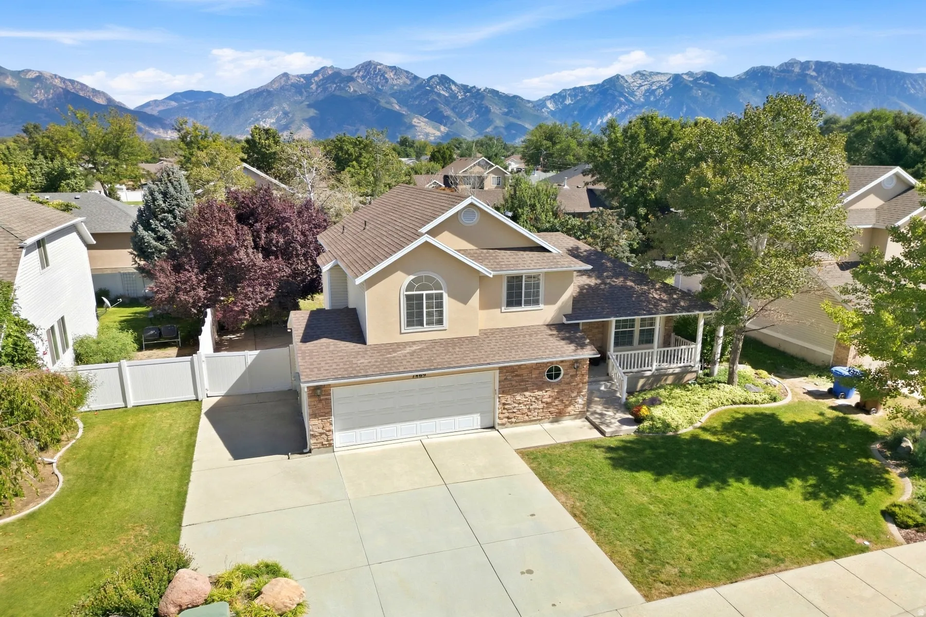 Stucco and stone exterior with an attached garage, covered front porch, and mature landscaping