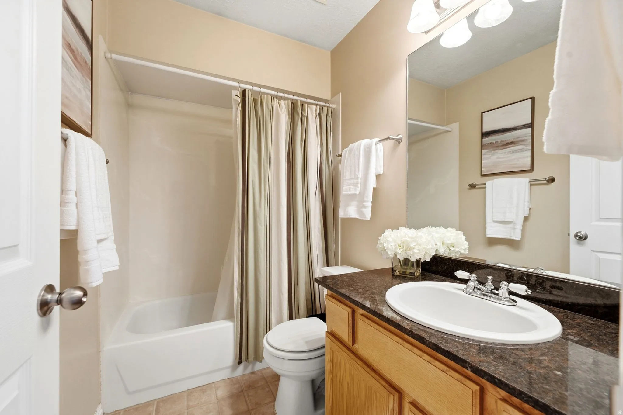 Bathroom featuring a bathtub with shower surround, wood-finish vanity with an integrated sink, and a dark stone-finish countertop