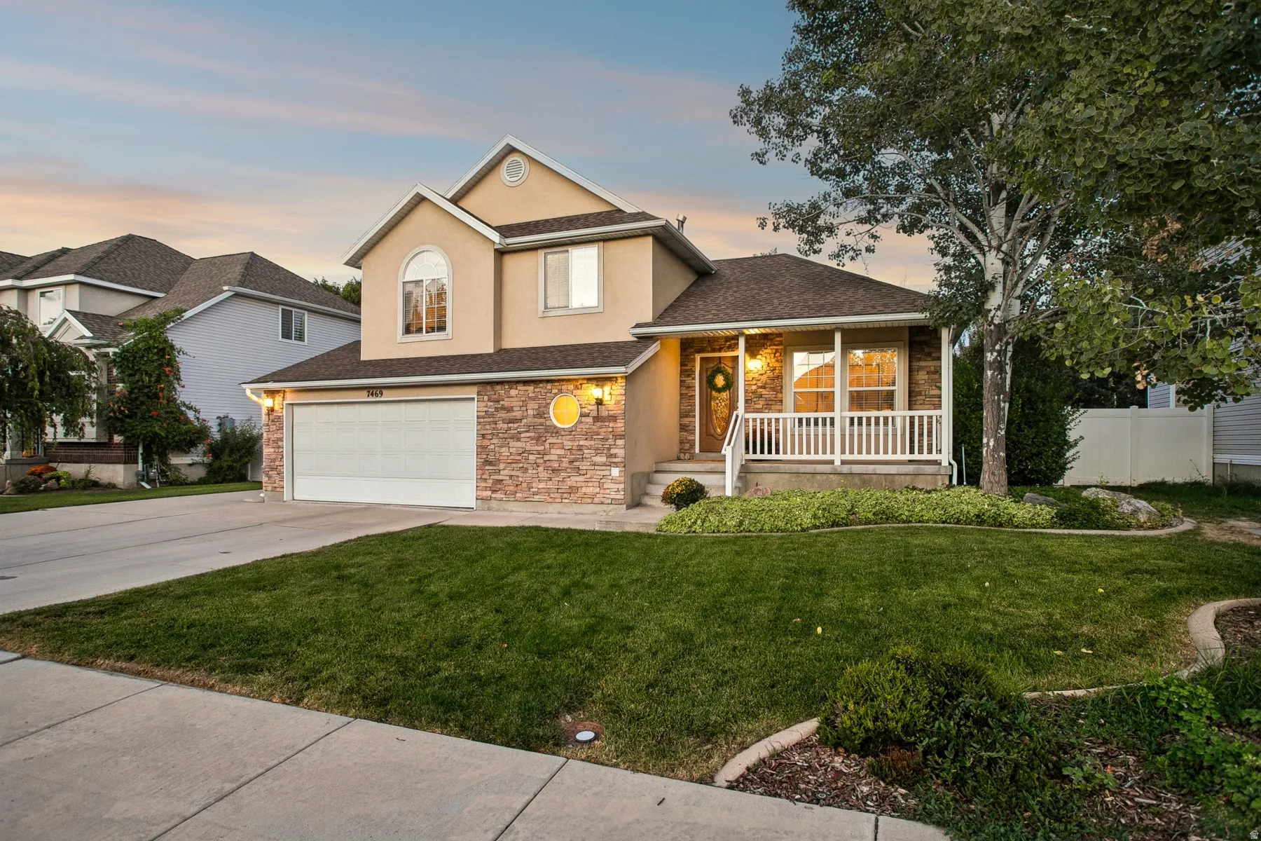 Two-story home featuring a brick and stone exterior with a covered front porch, two-car garage, and manicured landscaping