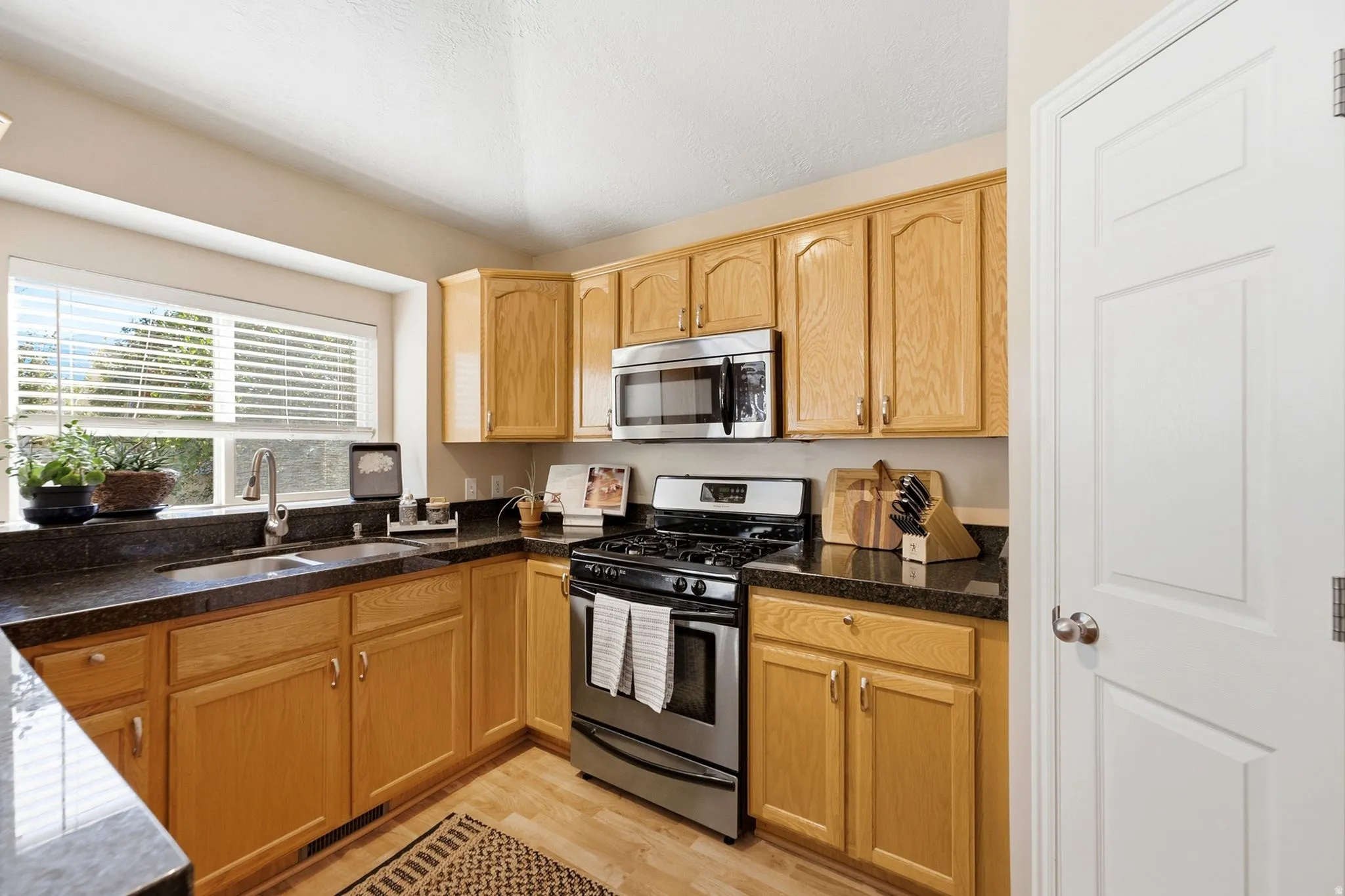 Kitchen featuring wood-finish cabinetry, dark countertops, stainless steel appliances, and wood-finish flooring
