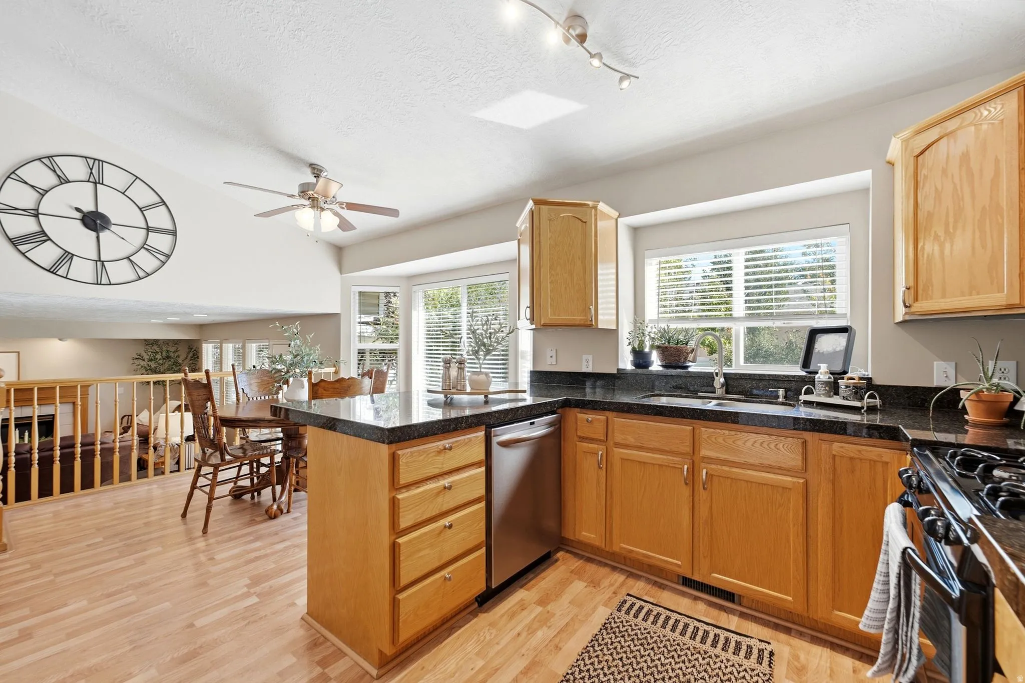Kitchen with wood-finish flooring, wood cabinetry, dark countertops, and stainless steel appliances. Abundant windows and light!