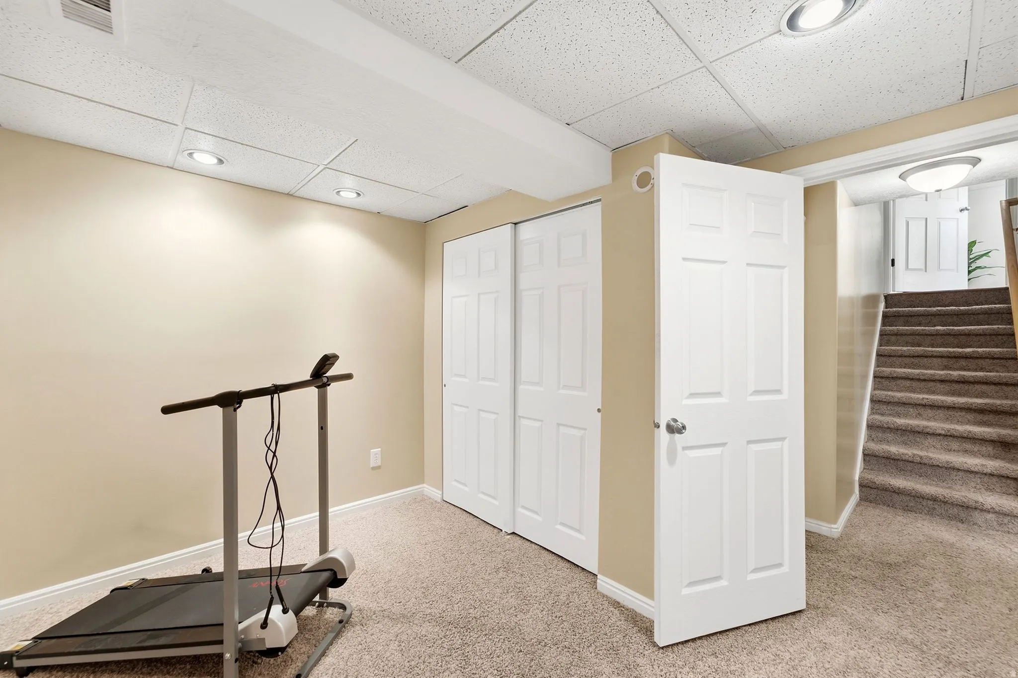 Recessed ceiling lighting, white bi-fold closet doors, white six-panel door, carpeted flooring, and a carpeted staircase