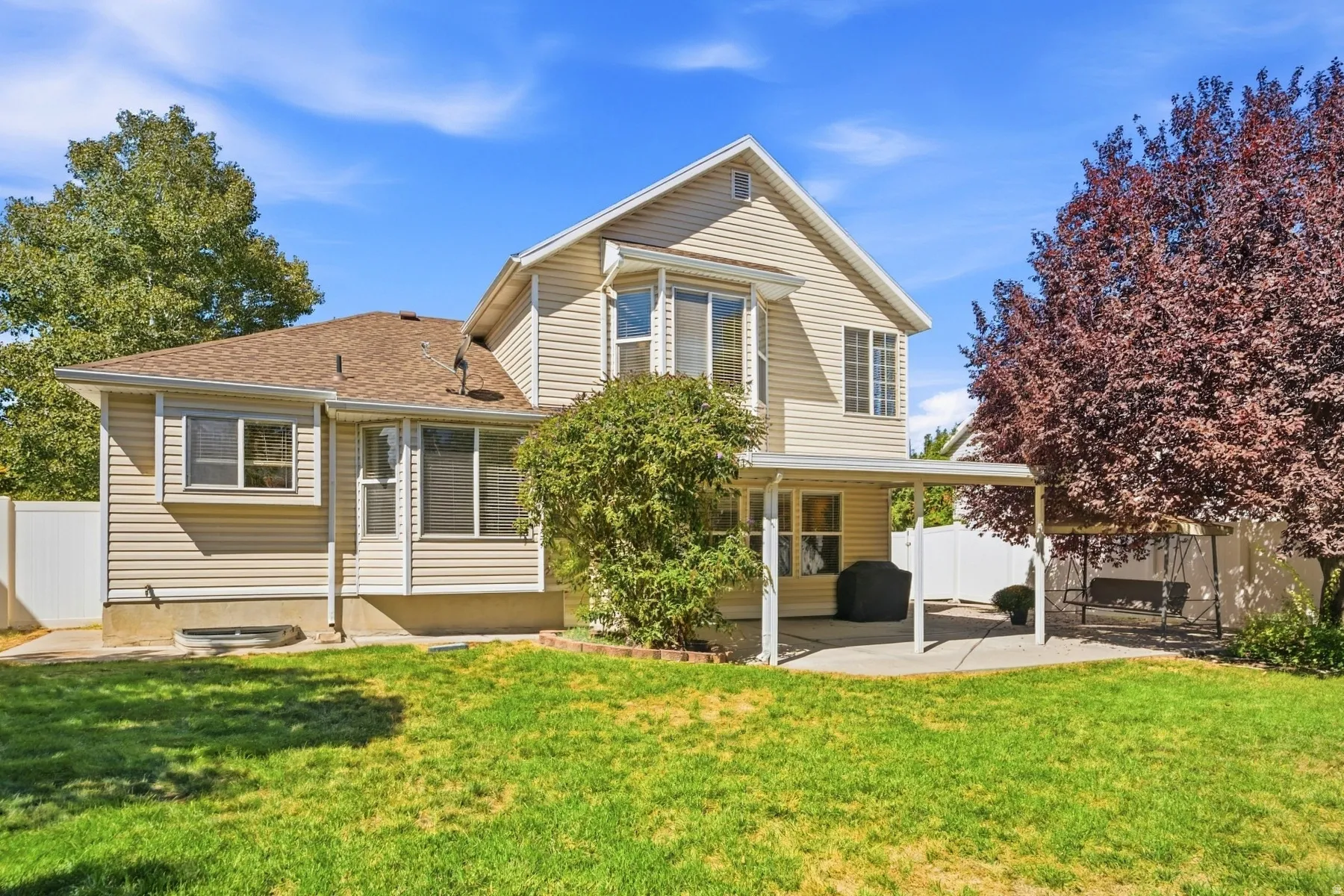 Expansive backyard featuring a manicured lawn, established trees, a covered patio, and privacy fencing