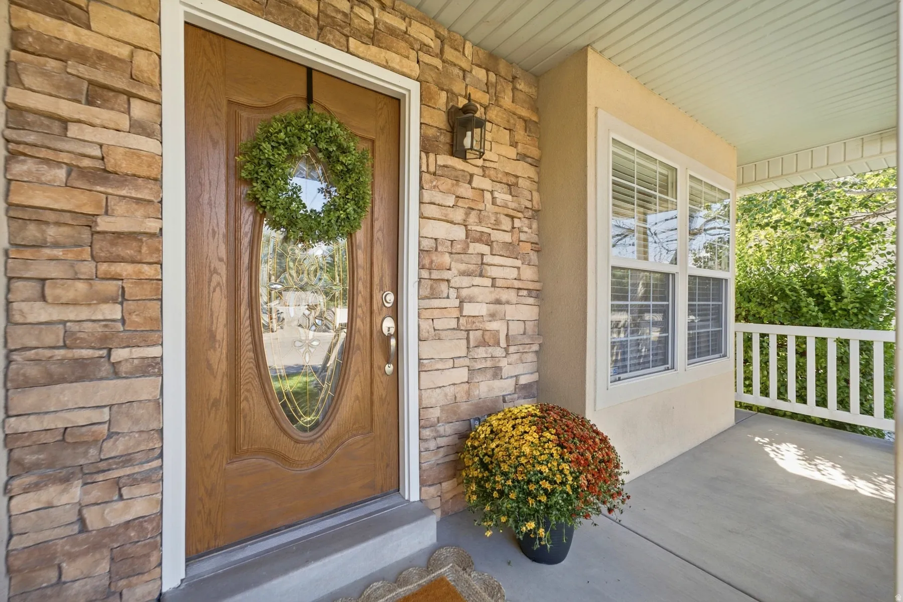 Stone veneer facade with an oval-lite entry door, a covered concrete porch, and a white spindle railing
