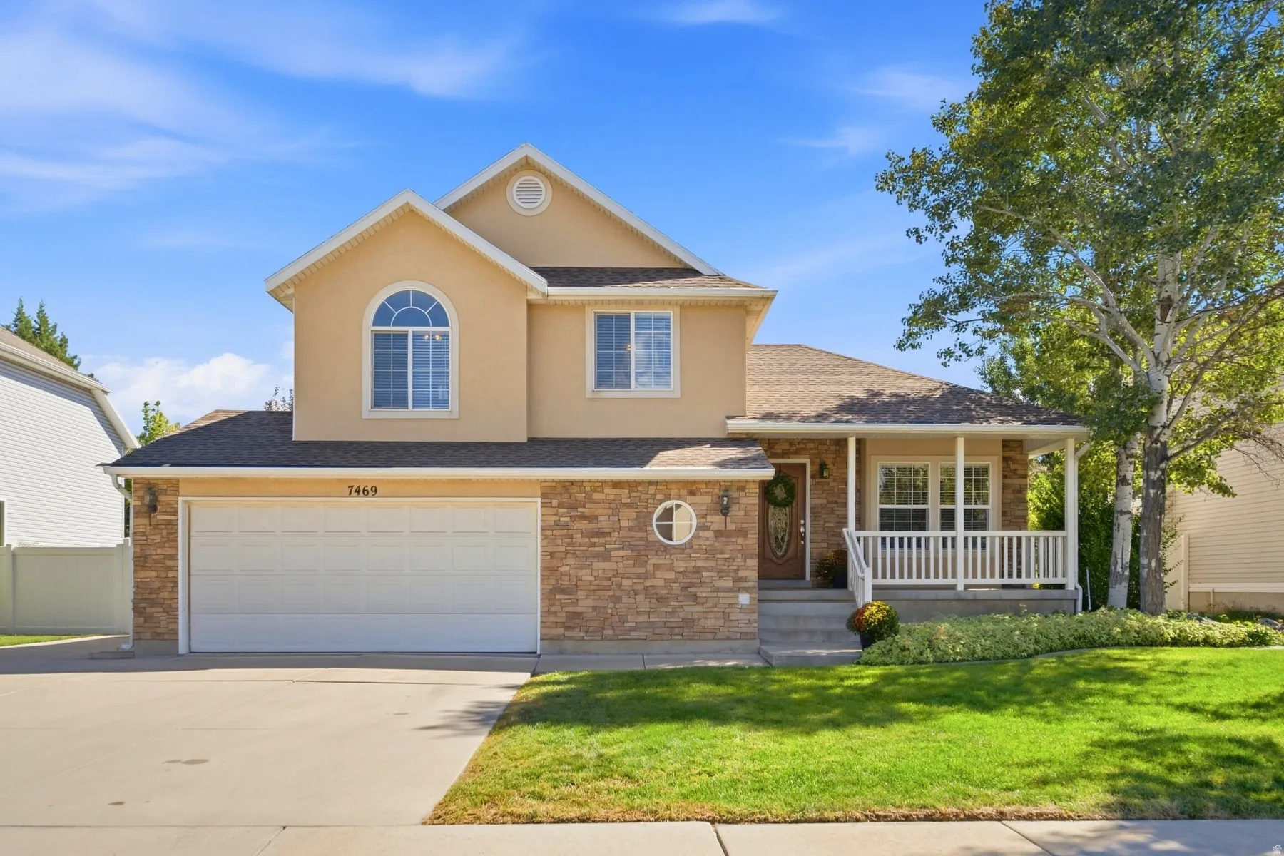Stucco and stone exterior, covered front porch, arched window, attached two-car garage, and a manicured lawn