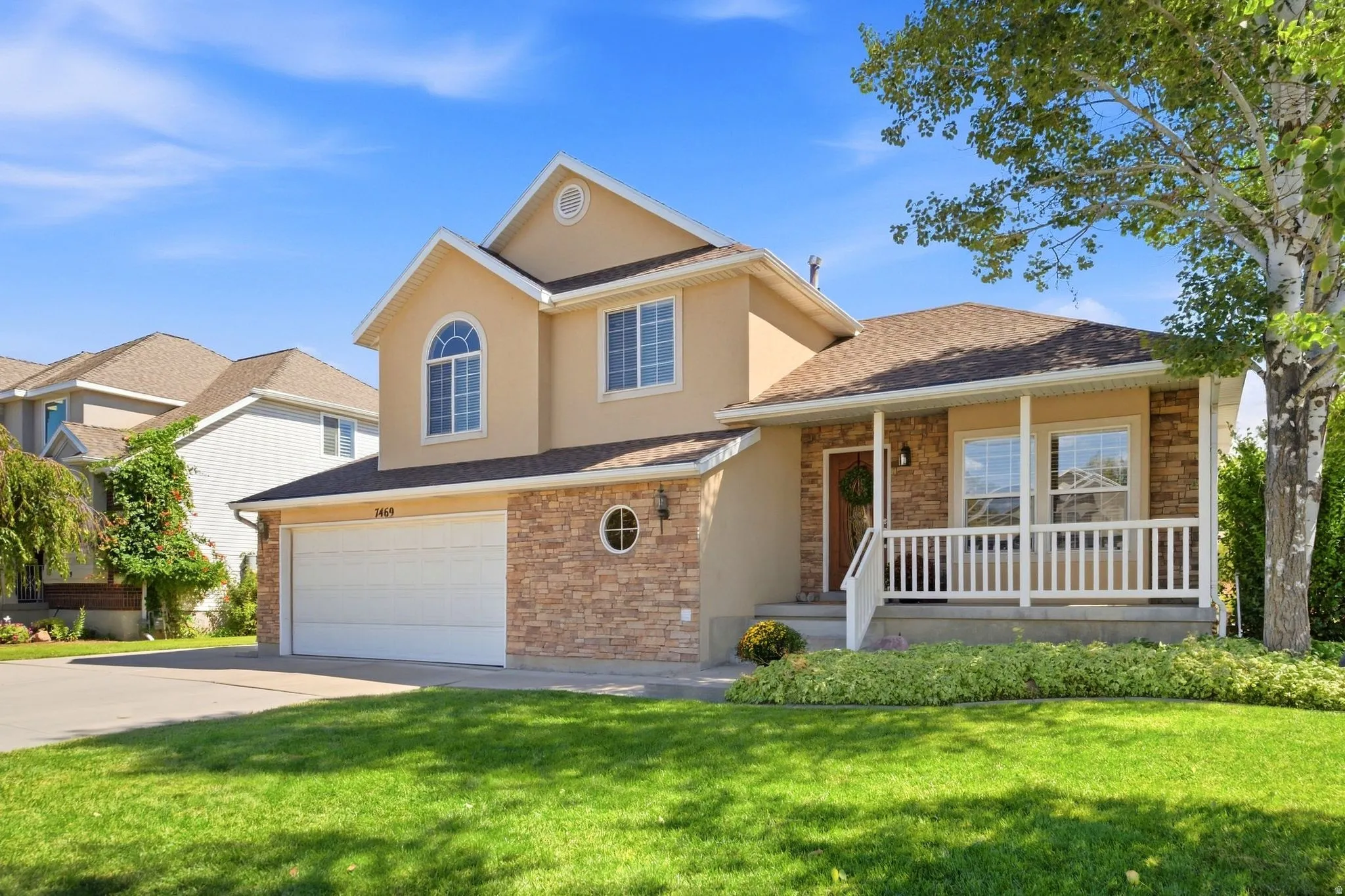 Tri-level residence featuring a stucco and stone veneer exterior, an attached two-car garage, and a covered front porch with white railings