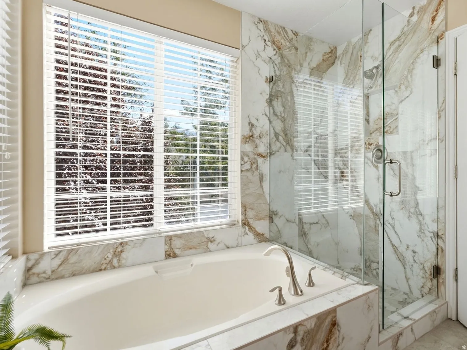 Primary ensuite bathroom features a soaking tub with brushed nickel fixtures, a glass-enclosed shower with tile surround, and a large window with horizontal blinds