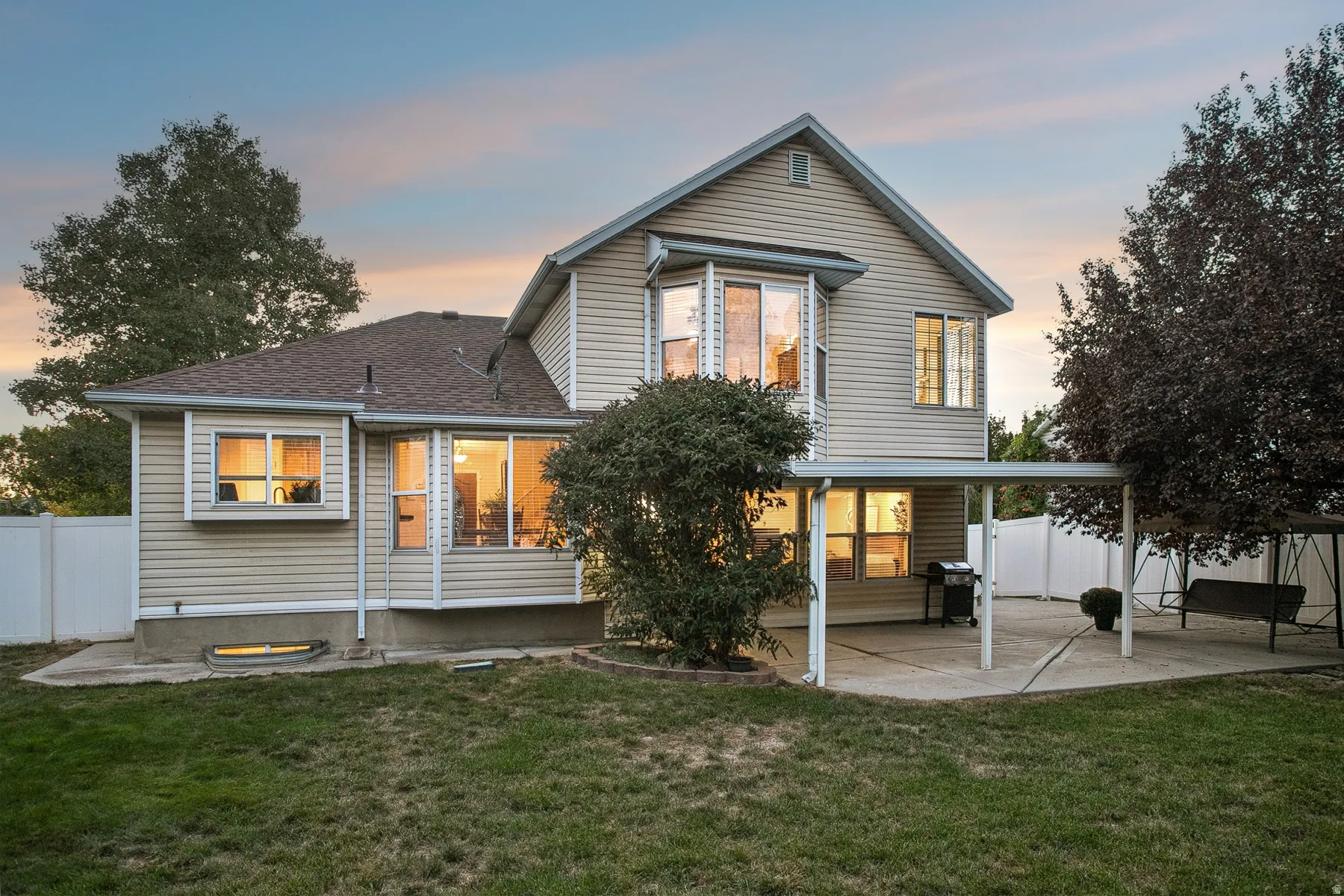 Expansive backyard with a manicured lawn, covered patio, and large mature trees