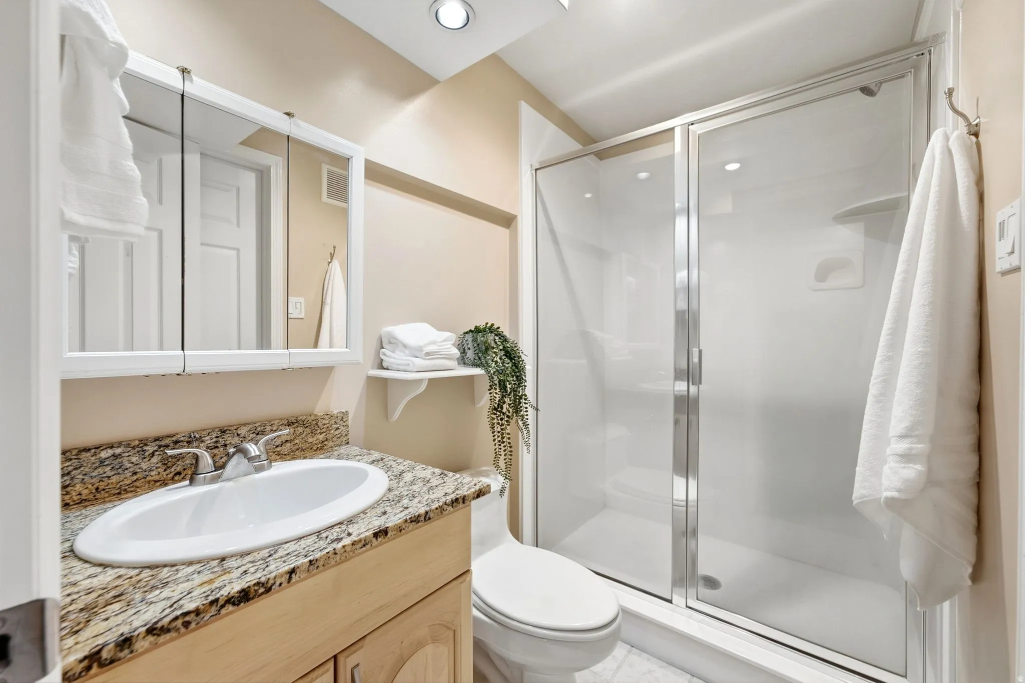 Vanity with a granite countertop and undermount sink, mirrored medicine cabinet, and a walk-in shower with clear glass enclosure
