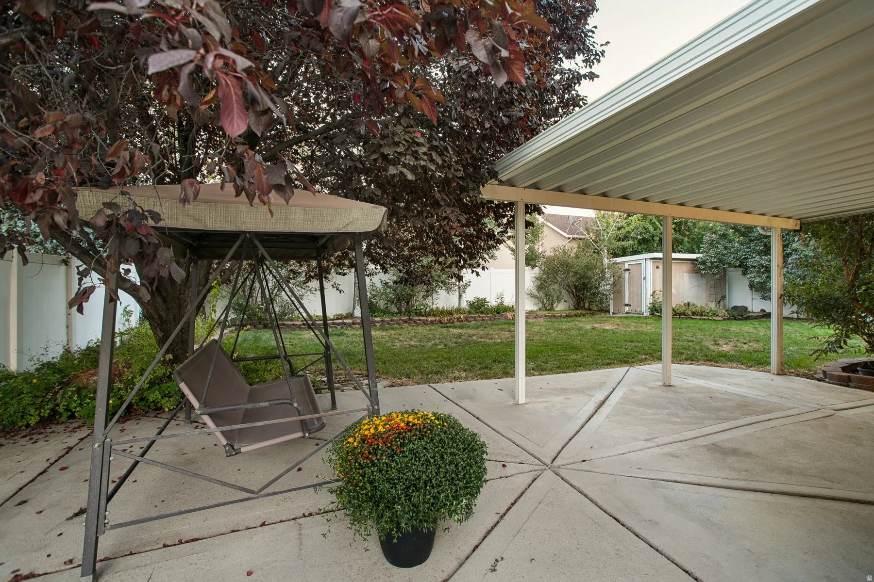 Covered patio with concrete flooring, expansive lawn, and mature trees