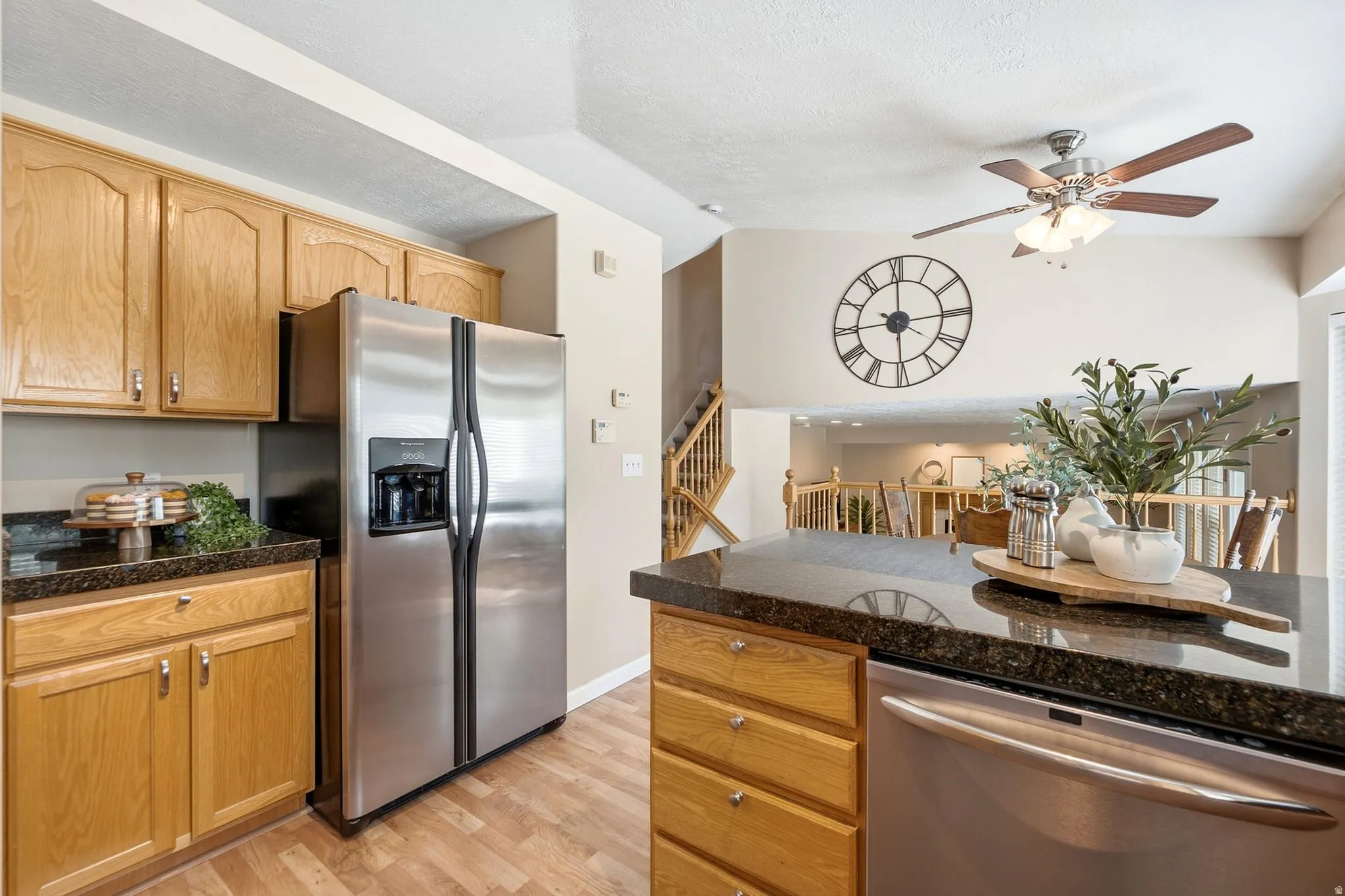 Kitchen featuring wood cabinetry, stainless steel appliances, dark stone countertops, wood-finish flooring, and a ceiling fan with light fixture