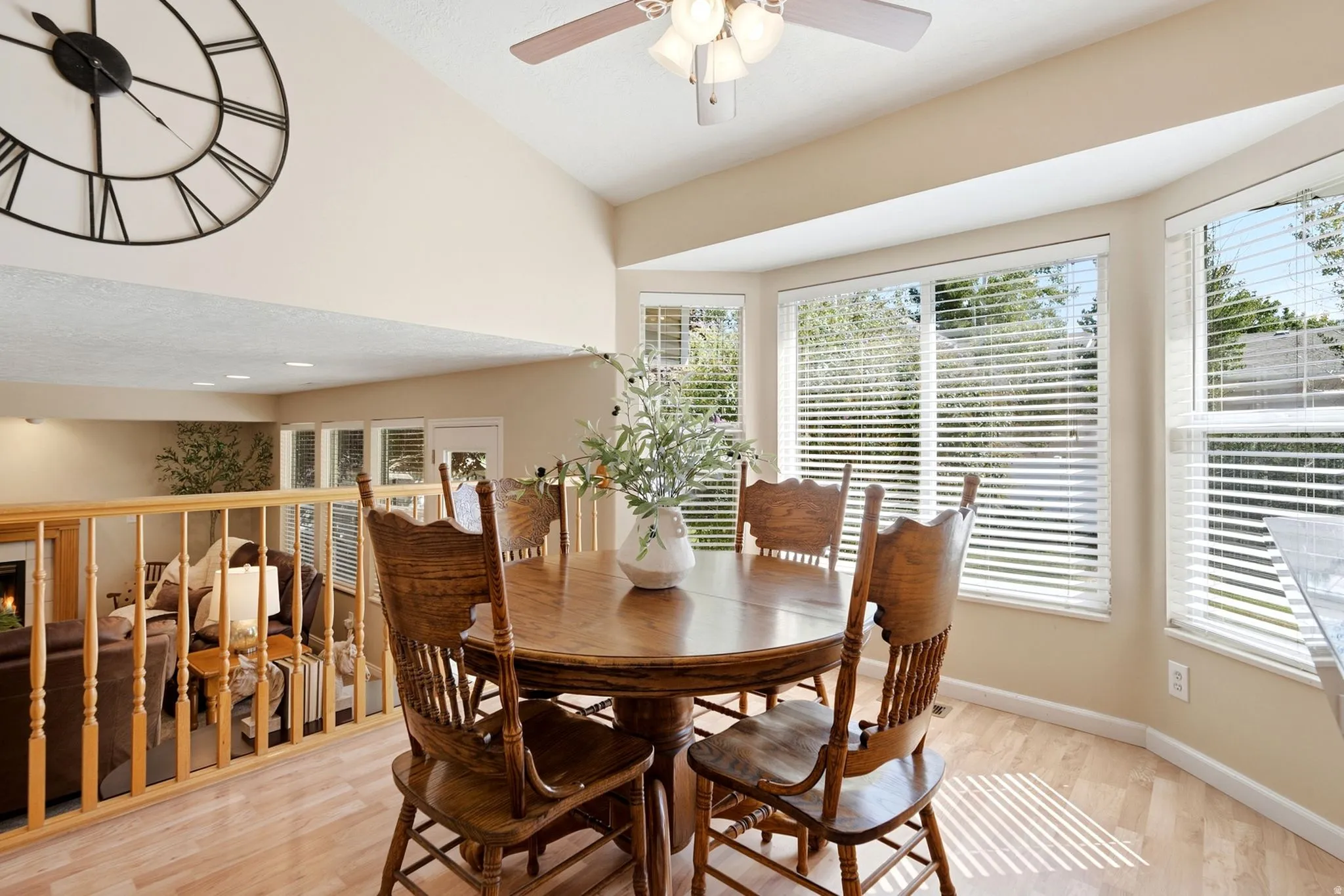 Vaulted ceiling with a ceiling fan, bay window configuration, wood-finish flooring, and a wood railing