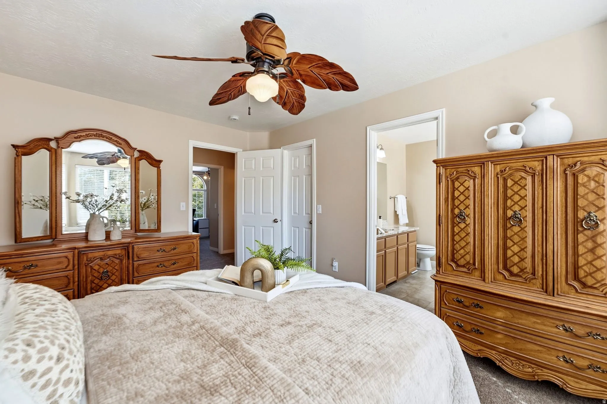 Overhead ceiling fan with leaf-shaped blades, light beige wall paint, white trim, and a visible doorway to an adjacent bathroom featuring a double vanity