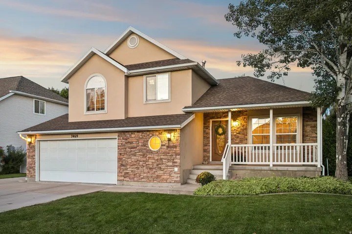Tri-level residence featuring a stucco and stone veneer exterior, an attached two-car garage, and a covered front porch with white railings
