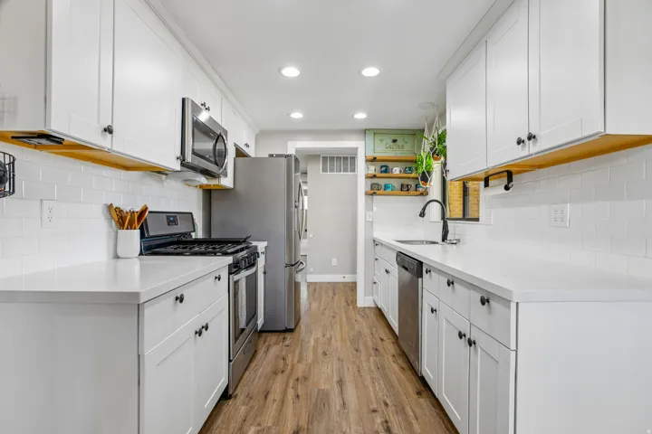 White cabinetry with black hardware, white subway tile backsplash, stainless steel appliances, light-toned countertops, and wood-finish flooring