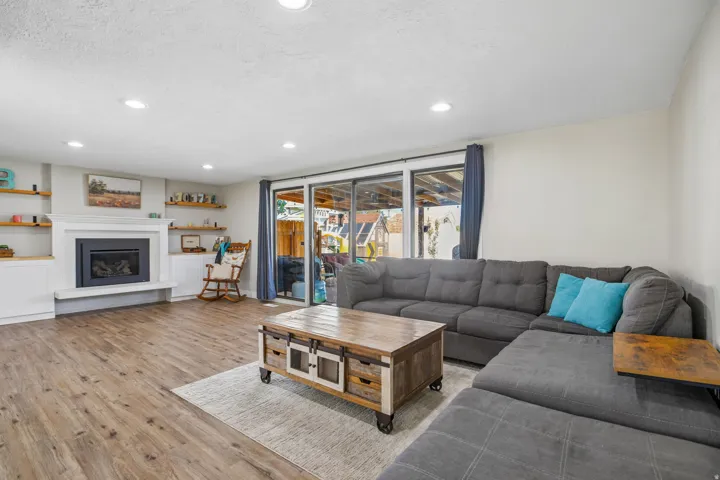 Wood-finish flooring throughout, featuring a built-in fireplace with white mantel, recessed lighting, built-in shelving, and sliding glass doors