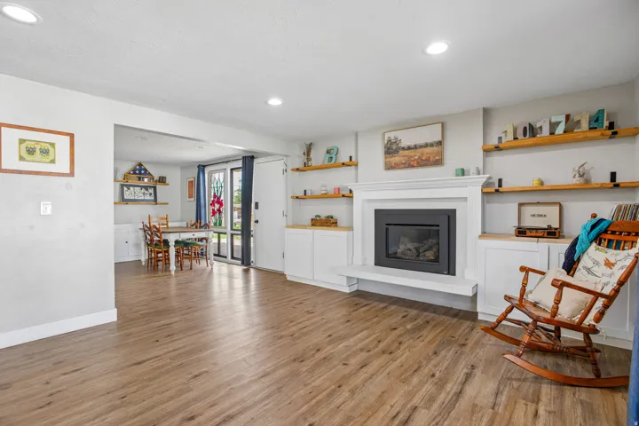 Wood-finish flooring throughout, featuring a fireplace with a white mantel and hearth, recessed lighting, built-in cabinetry, and open shelving