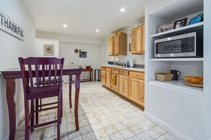 Recessed lighting illuminates the space, featuring wood cabinetry, a built-in microwave, and a stainless steel sink