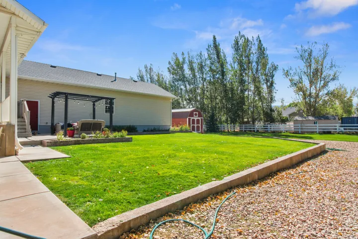 Expansive lawn with a gravel driveway, white picket fencing, and a red auxiliary shed