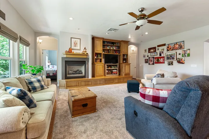 Gas fireplace with a wood mantel, built-in entertainment center, recessed lighting, ceiling fan, and carpeted flooring