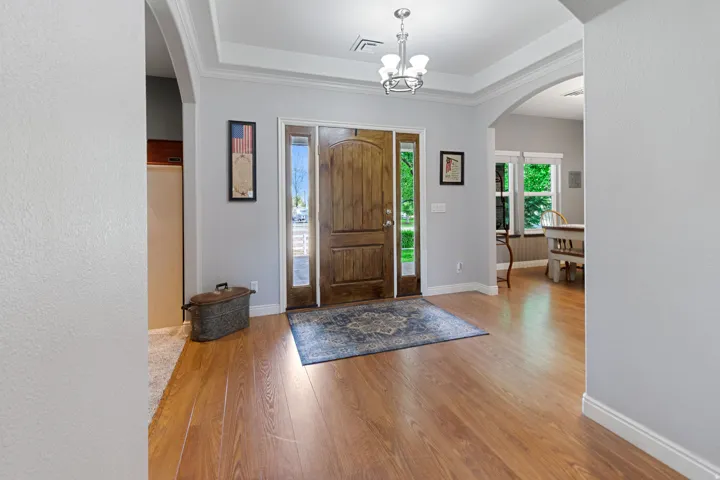 Wood-finish flooring, recessed tray ceiling with crown molding, archways, and a multi-paneled wood front door with sidelight windows
