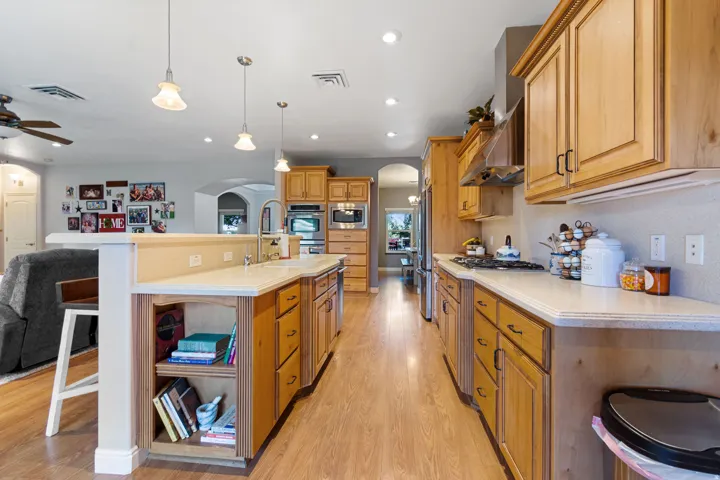 Kitchen featuring wood-finish flooring, recessed lighting, pendant lighting, built-in stainless steel appliances, and wood cabinetry