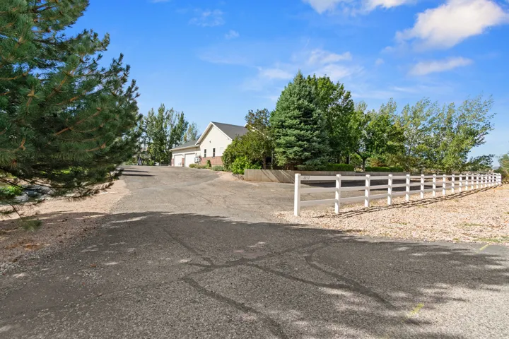 Paved driveway leading to a residence with a two-car garage, surrounded by mature trees and a white post-and-rail fence