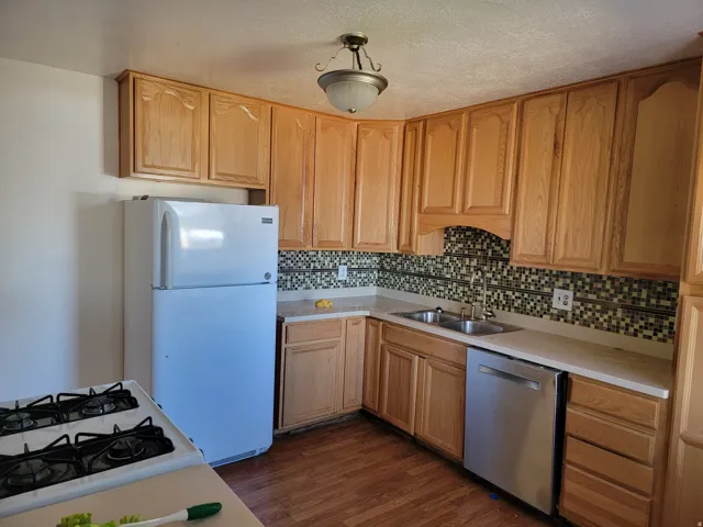 Kitchen featuring wood-finish cabinetry, mosaic tile backsplash, stainless steel dishwasher, and a double basin sink