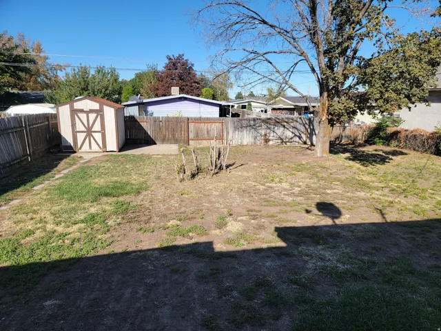 Enclosed backyard featuring a storage shed, concrete pad, and mature tree