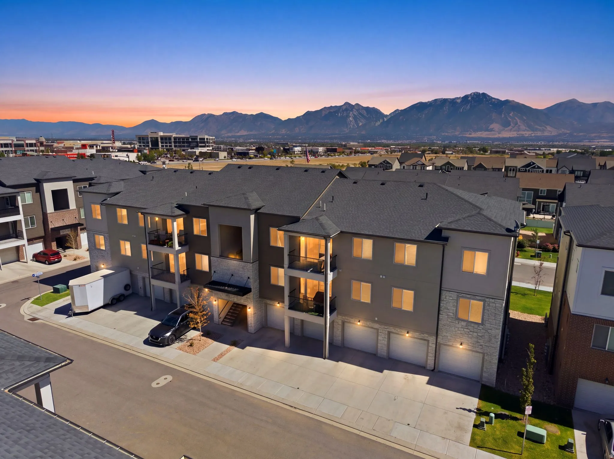 Contemporary multifamily structure featuring stone and stucco exterior finishes, multiple private balconies, attached garages, and a dark shingle roof