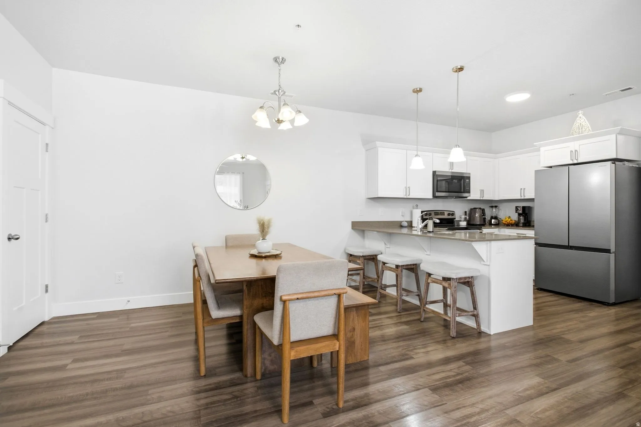 Open concept living space featuring wood-finish flooring, white kitchen cabinetry, stainless steel appliances, and pendant lighting