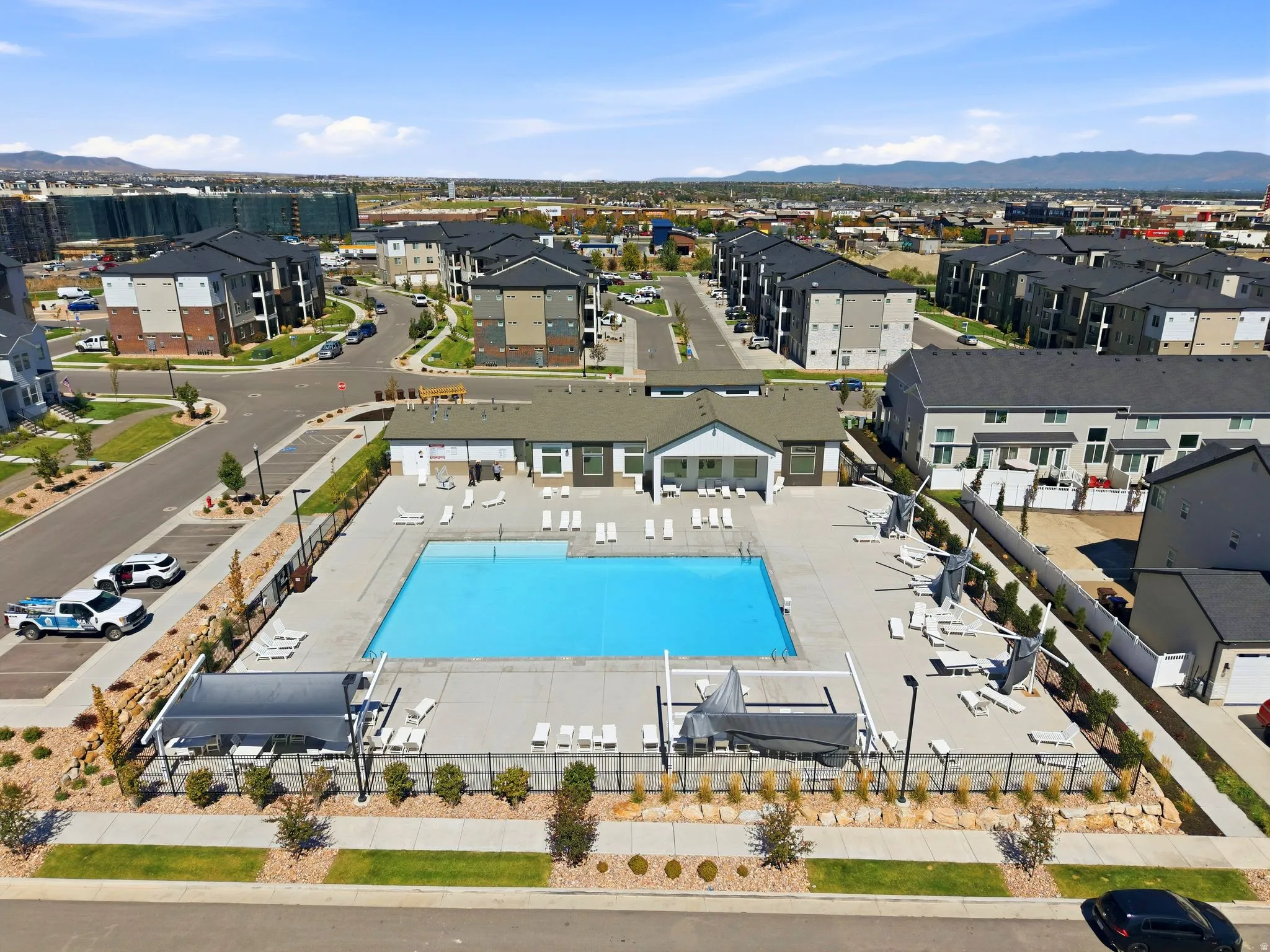 Community swimming pool with surrounding concrete deck, flanked by lounge seating and shade structures