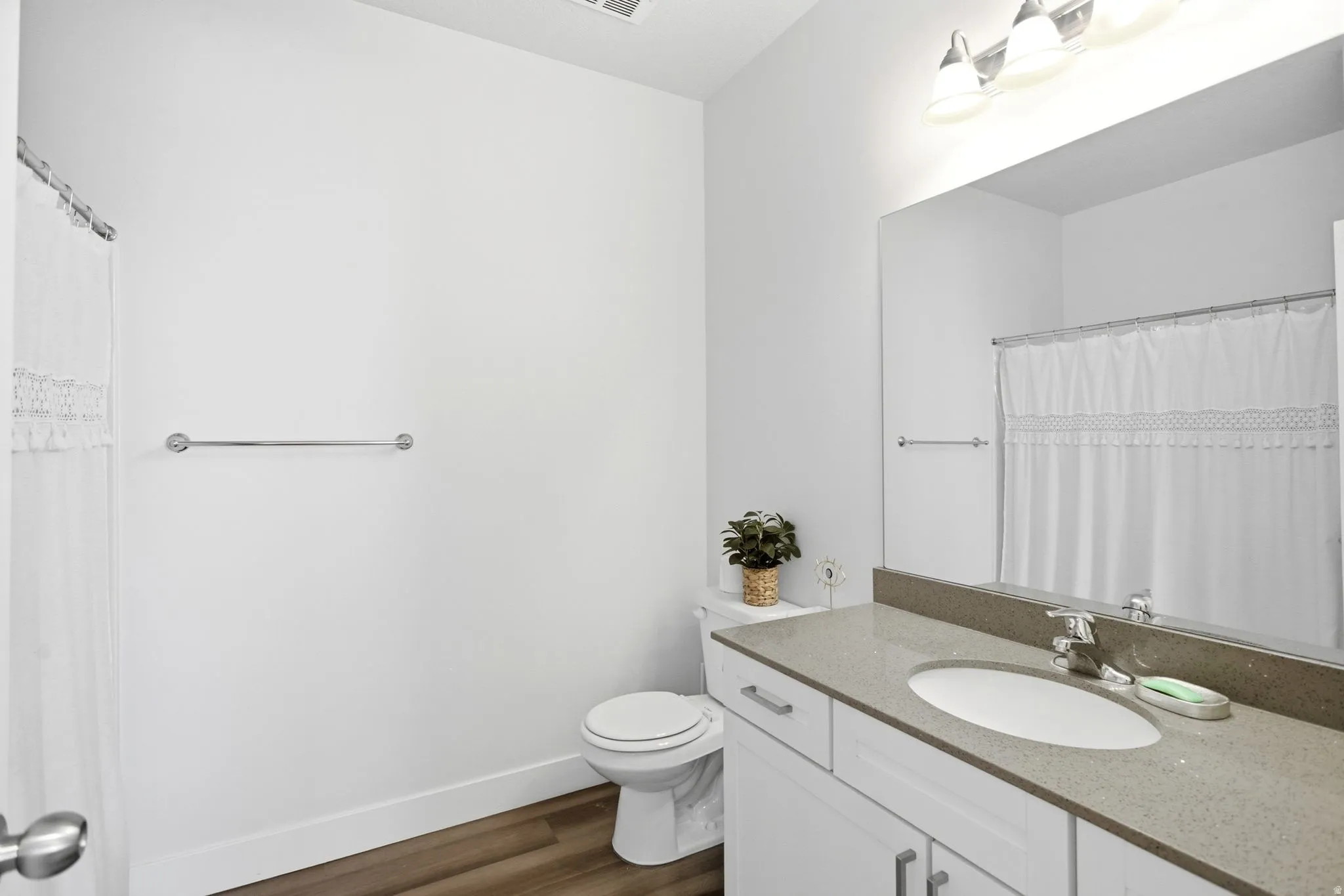 Bathroom featuring wood-finish flooring, a vanity with white cabinetry, a single basin sink, a large wall-mounted mirror, and a three-light fixture