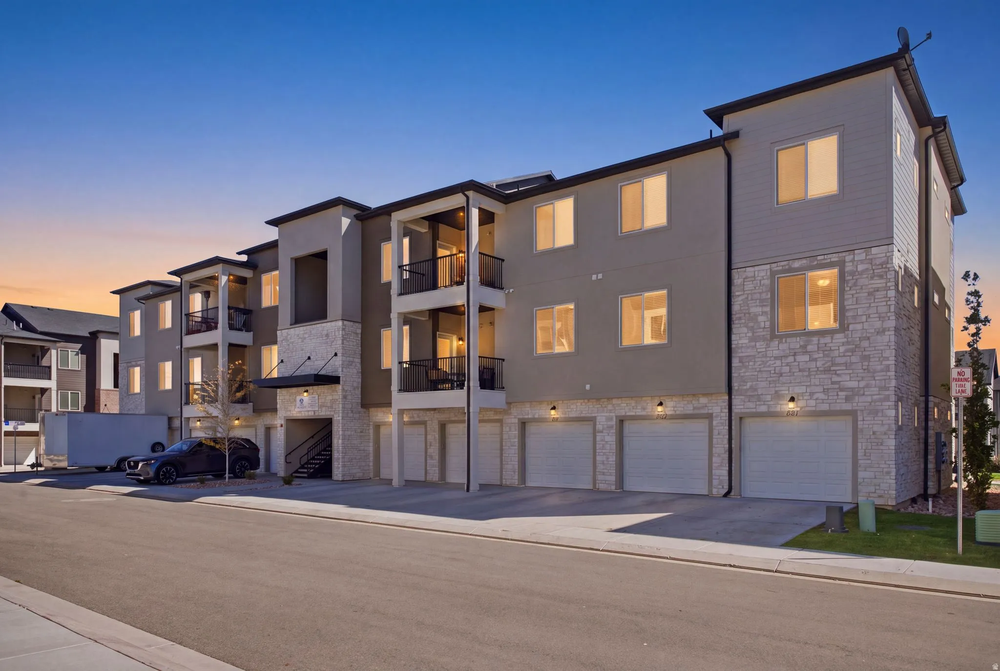 Contemporary multi-story building featuring stone veneer and horizontal siding accents, multiple balconies with dark railings, and ground-level garages