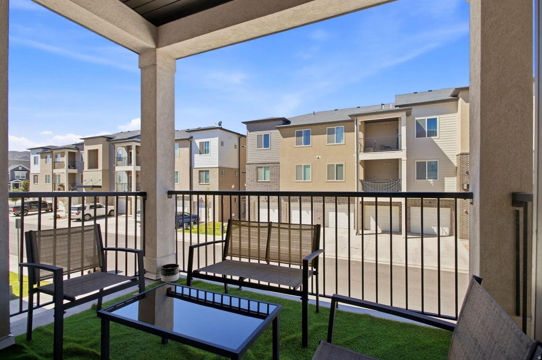 Balcony with black metal railings, textured columns, and a synthetic grass floor covering