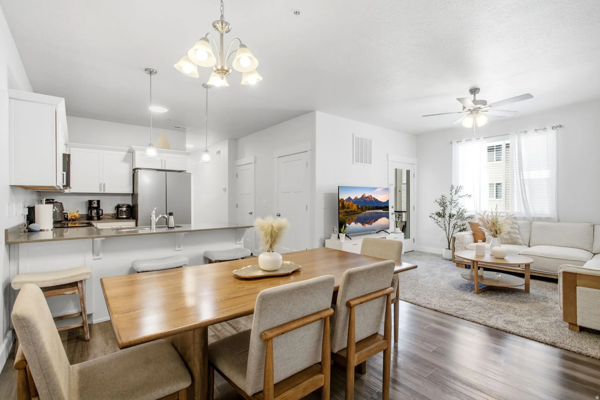 Open-concept living space featuring wood-finish flooring, white cabinetry, a kitchen island, pendant lighting, and a ceiling fan