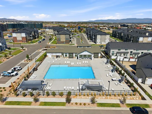 Community swimming pool with surrounding concrete deck, flanked by lounge seating and shade structures
