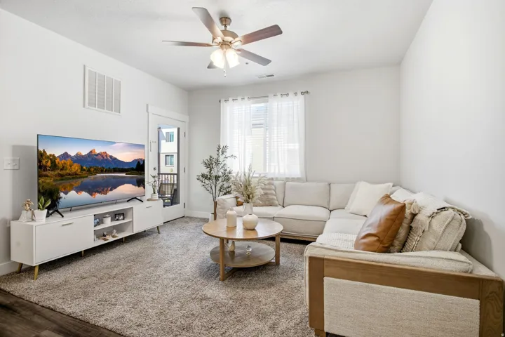 Wood-finish flooring, ceiling fan with integrated lighting, and a white interior door leading to an outdoor space