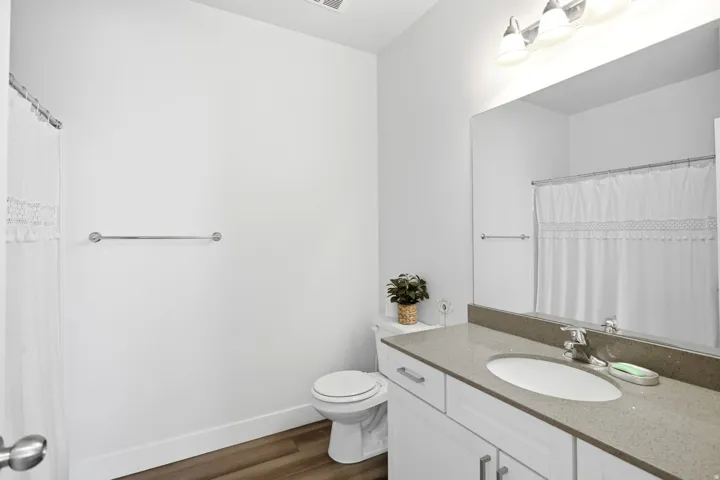 Bathroom featuring wood-finish flooring, a vanity with white cabinetry, a single basin sink, a large wall-mounted mirror, and a three-light fixture