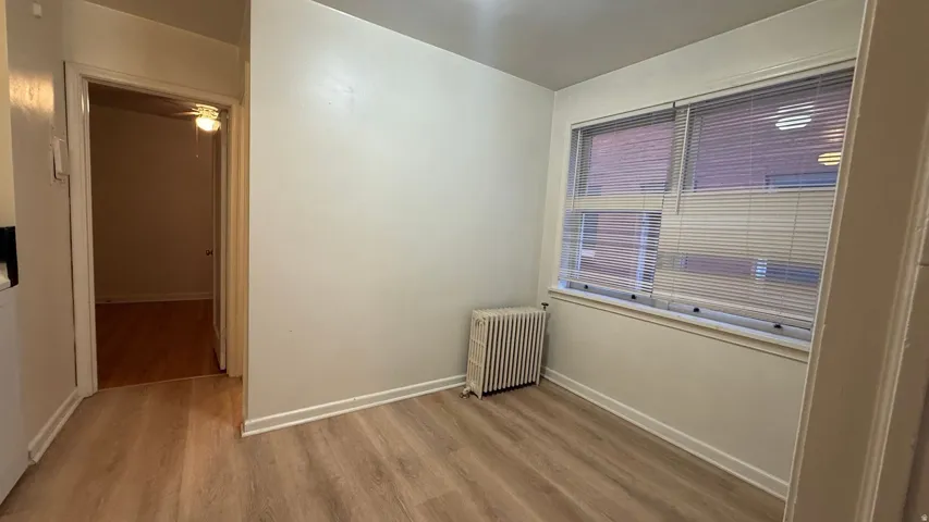 Wood-finish flooring throughout, multiple windows with horizontal blinds, and a classic radiator