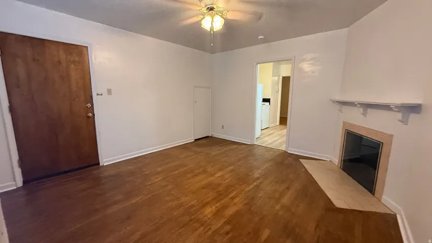 Hardwood-finish flooring, recessed fireplace, wall-mounted shelf, ceiling fan light fixture, and solid wood entry door