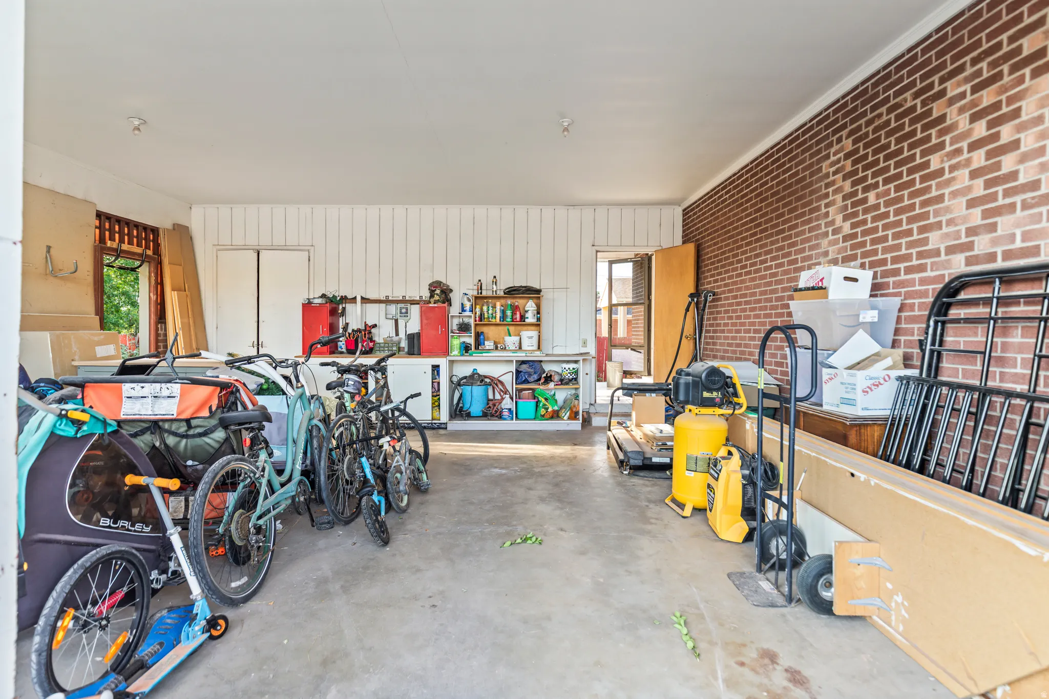 Attached garage featuring a concrete floor, exposed brick wall, and white paneled walls