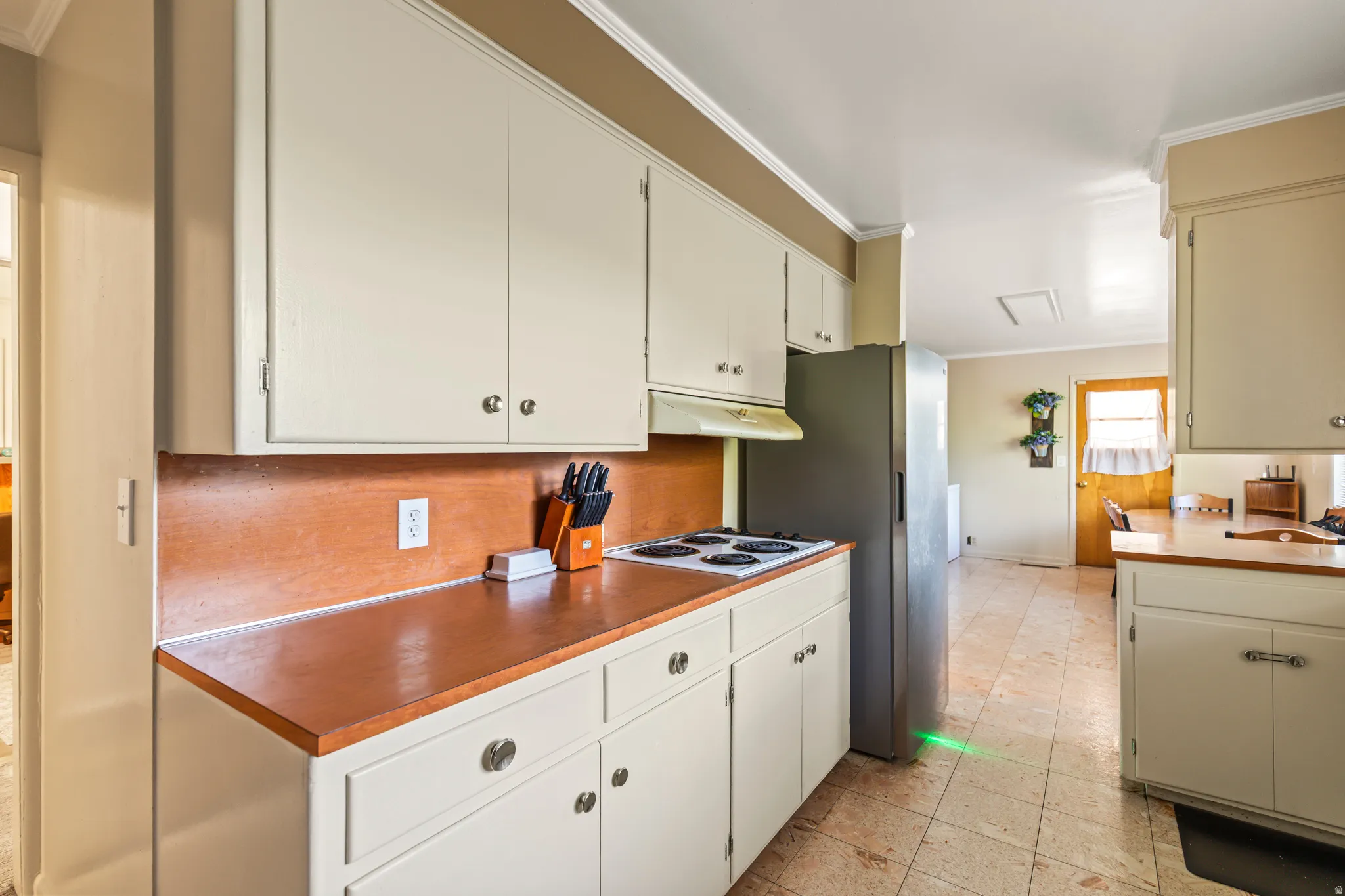 Kitchen with white cabinetry, wood-finish countertops, tile flooring, and a stainless steel refrigerator