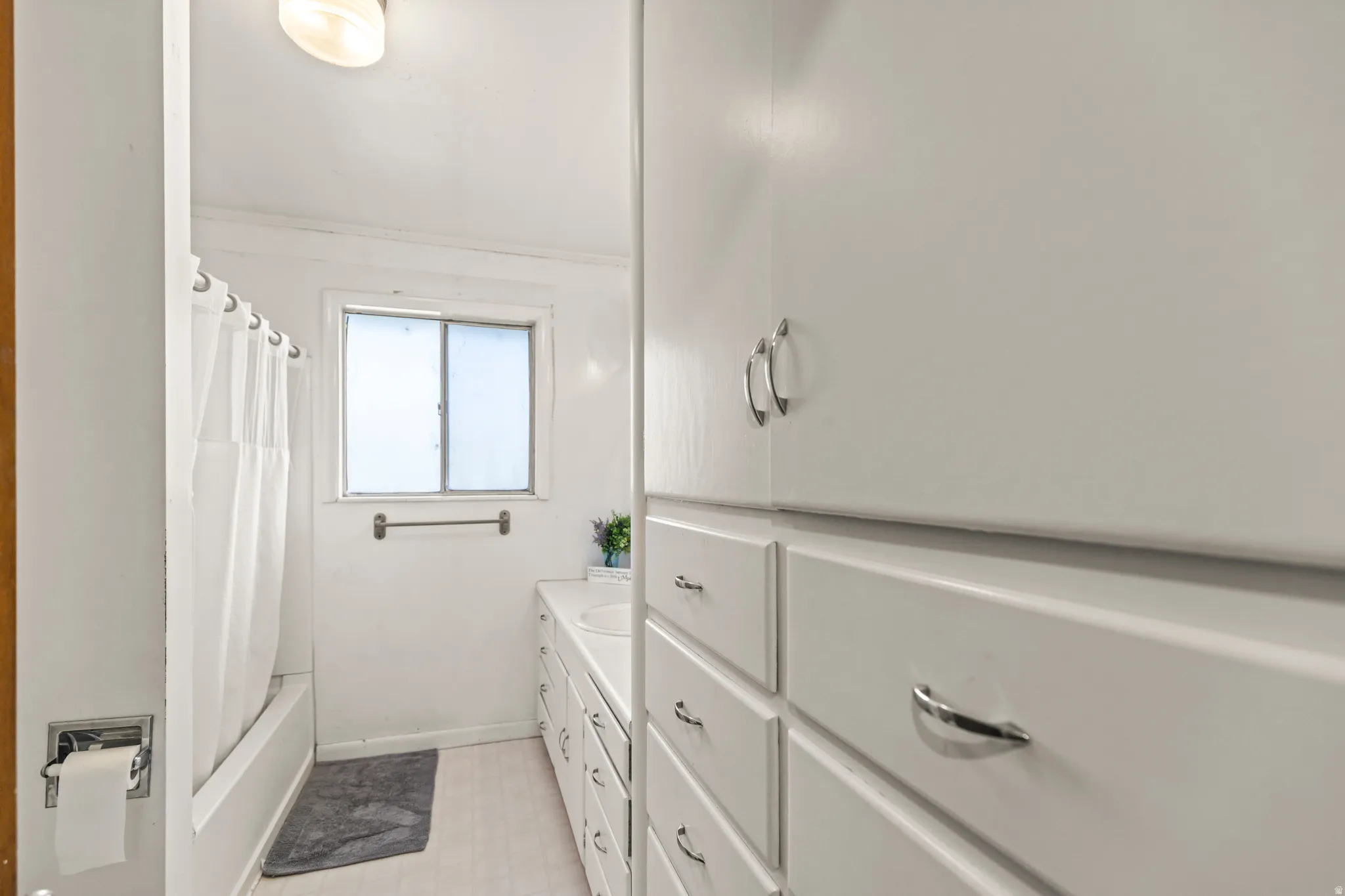 White vanity with integrated sink, extensive storage cabinetry, a privacy window, and a shower/tub combination
