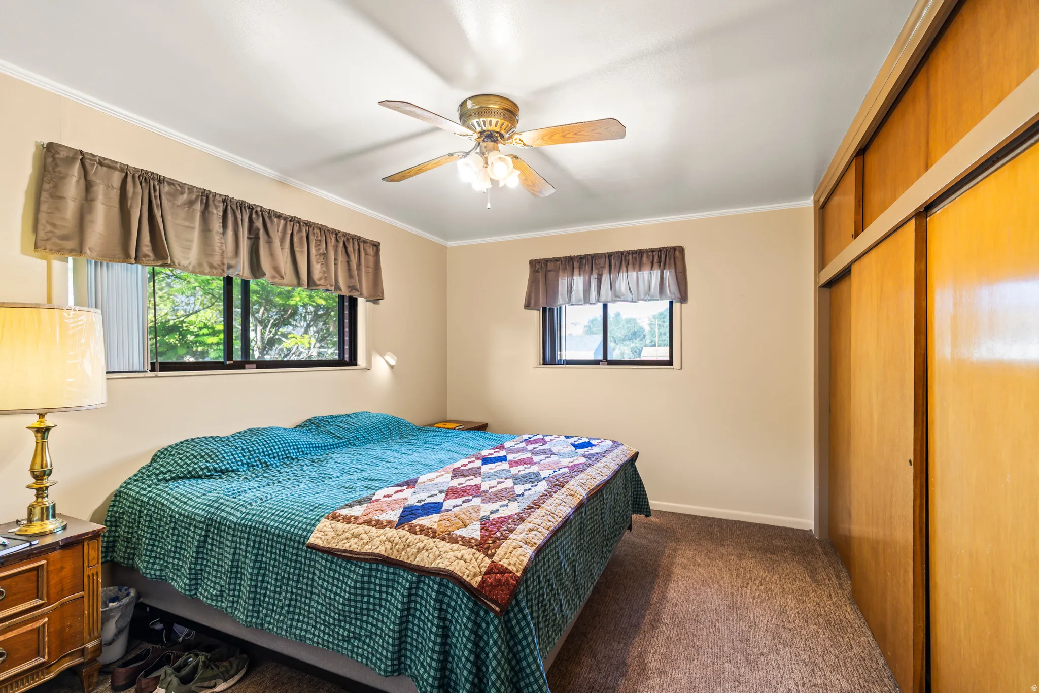 Carpeted room featuring dual windows, a ceiling fan with integrated lighting, and wood-finish sliding closet doors