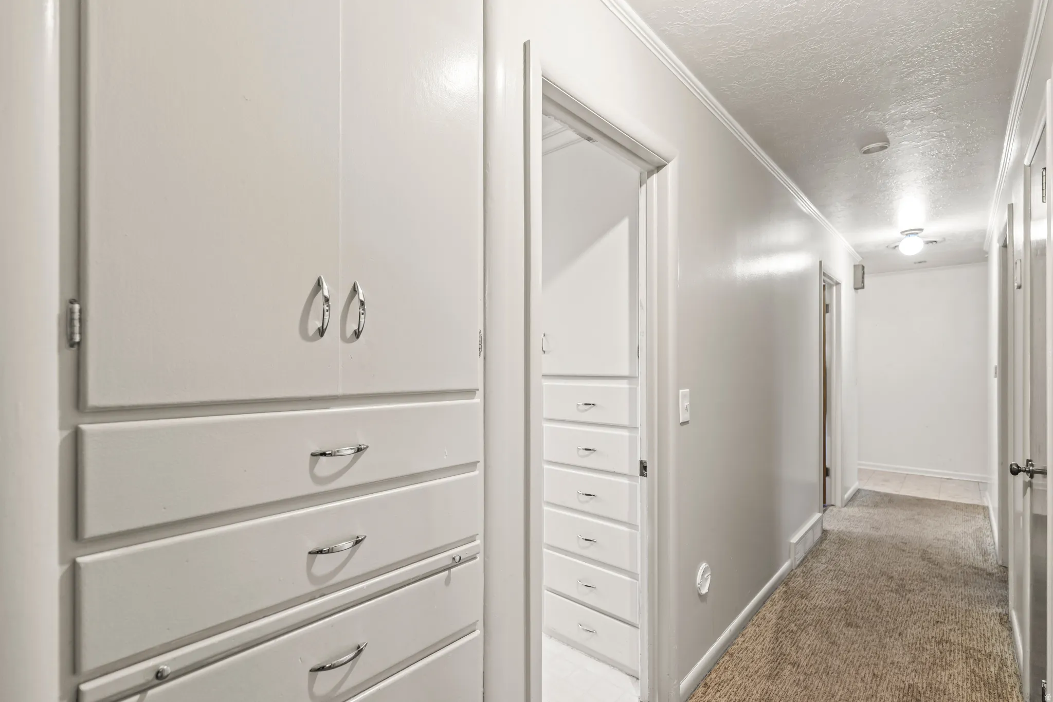 Hallway with built-in cabinetry featuring multiple drawers and upper cabinets, light-colored walls, and textured carpet flooring