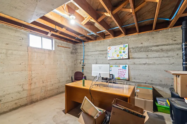 Exposed wood beam ceiling with visible plumbing, concrete walls, and a window