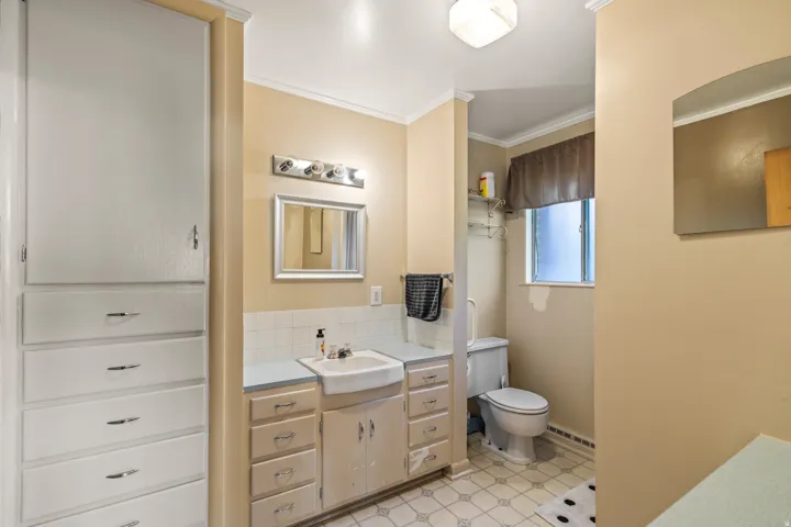 Built-in linen cabinet with multiple drawers, vanity with drop-in sink, wall-mounted light fixture, and window with privacy glass