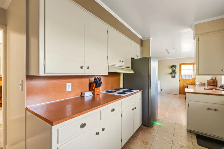 Kitchen with white cabinetry, wood-finish countertops, tile flooring, and a stainless steel refrigerator