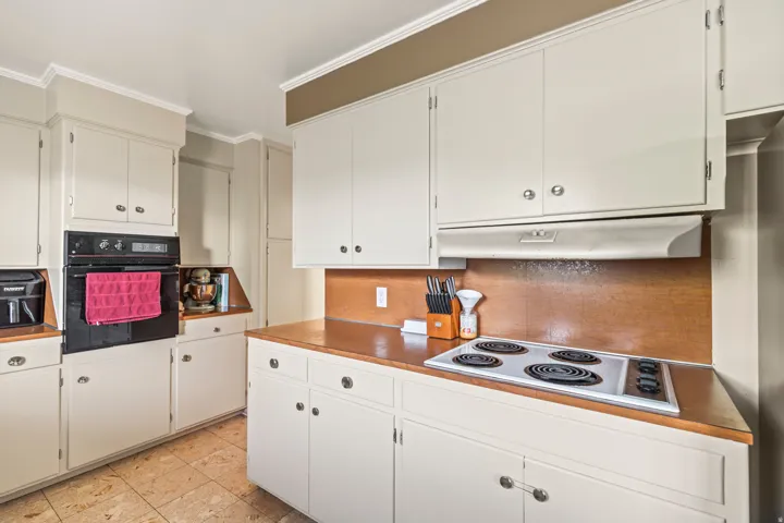 Built-in wall oven, electric cooktop, extensive cabinetry, wood-finish countertops, and tile flooring